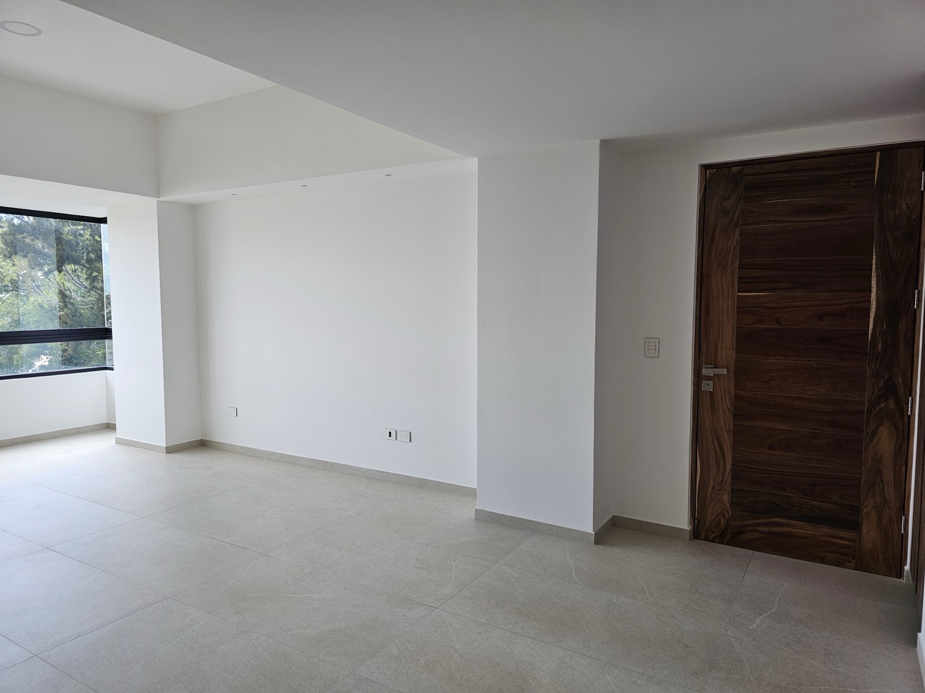 Estancia amplia con ventanales, piso gris y puerta de madera