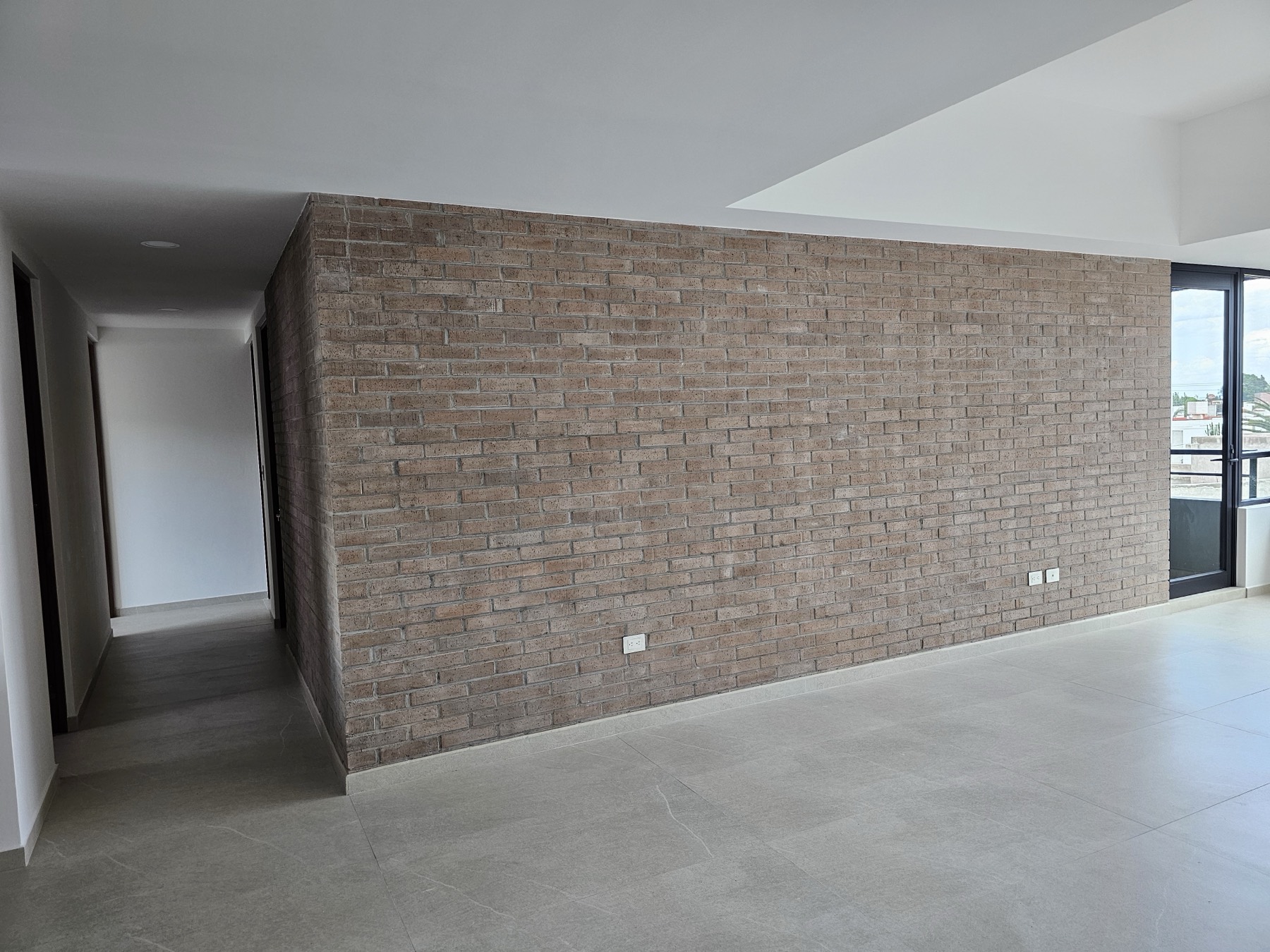 Estancia con muro de ladrillo y circulación hacia las recámaras