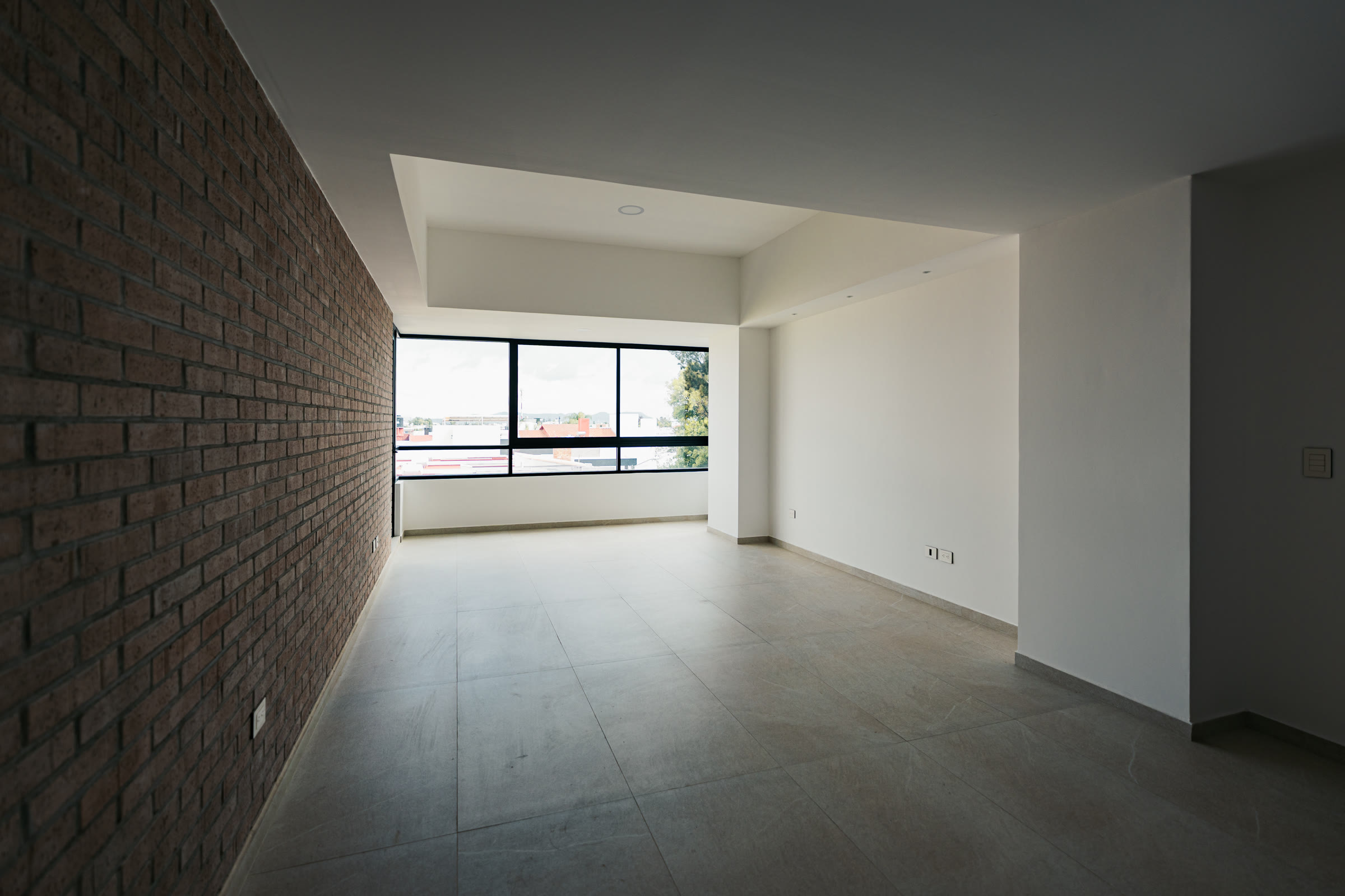 Sala comedor amplia con ventanal y muro de ladrillo