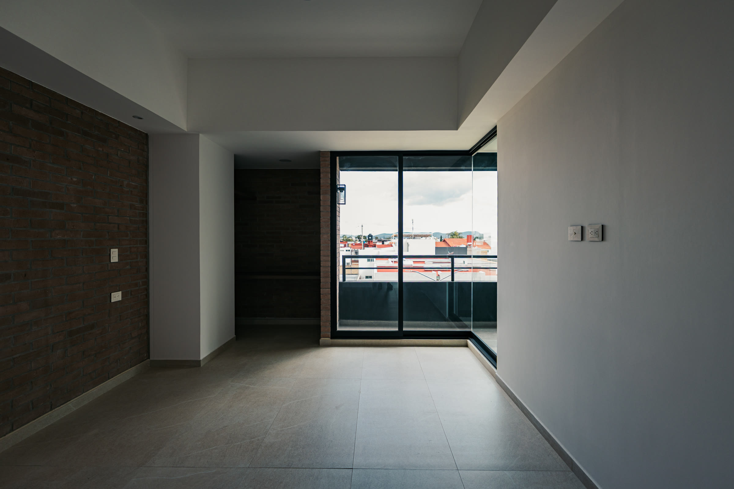 Recámara luminosa con muro de ladrillo y ventanal de piso a techo