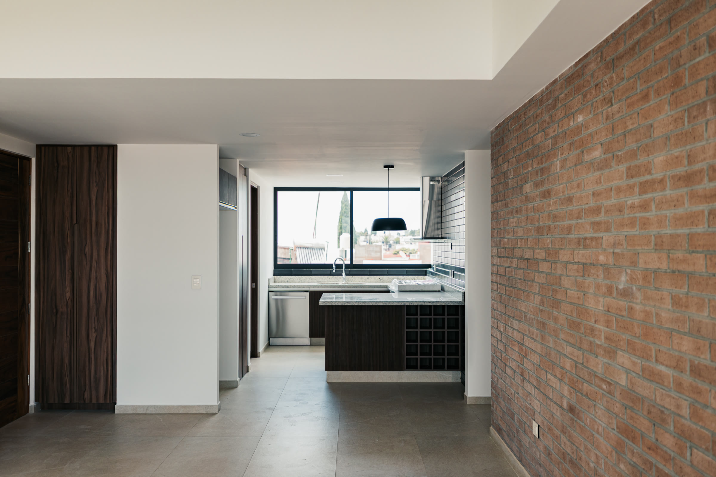 Cocina abierta conectada con un comedor y un muro de ladrillo